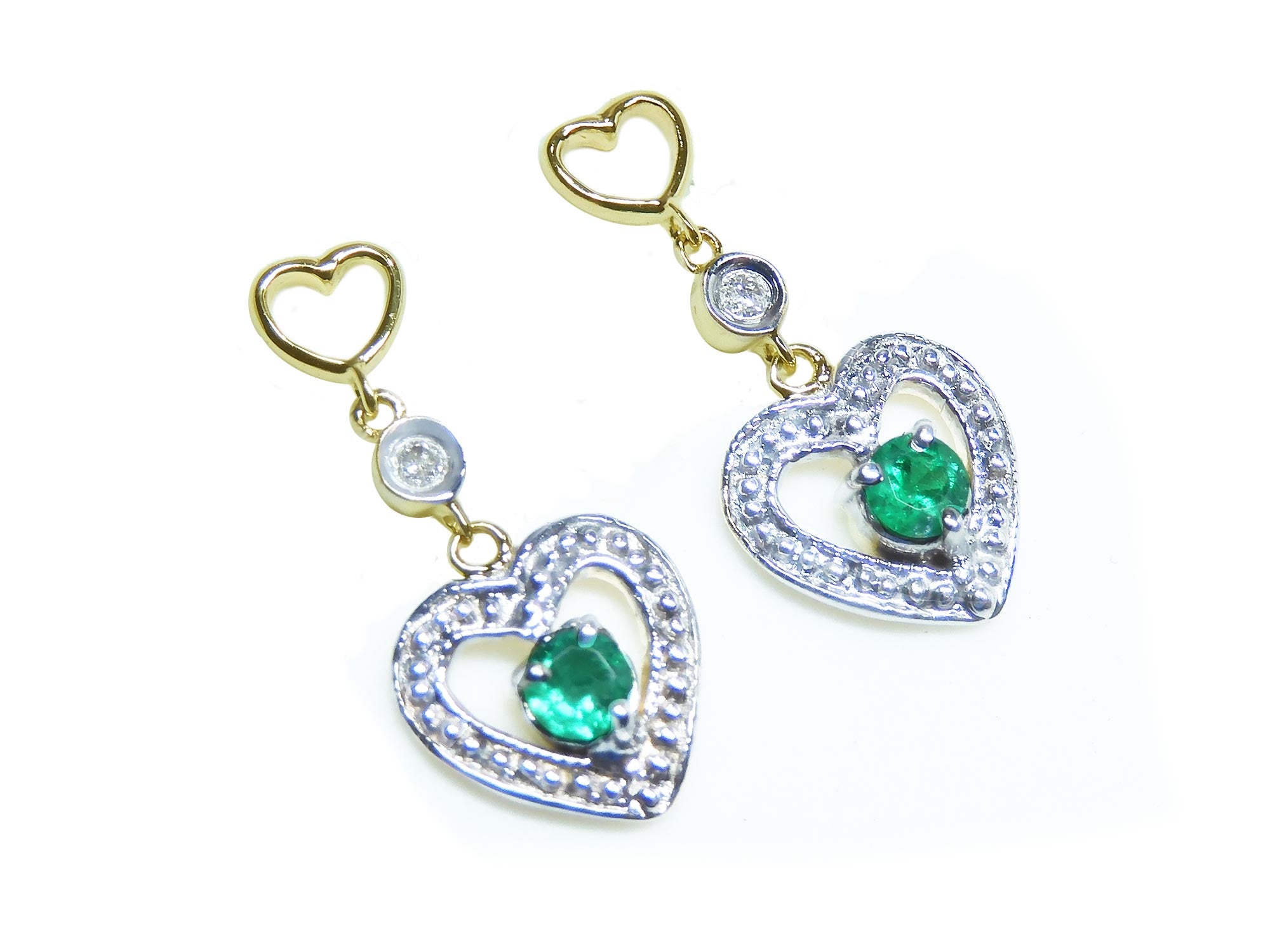 Pair of emerald heart earrings with round cut emeralds on a right position top view.