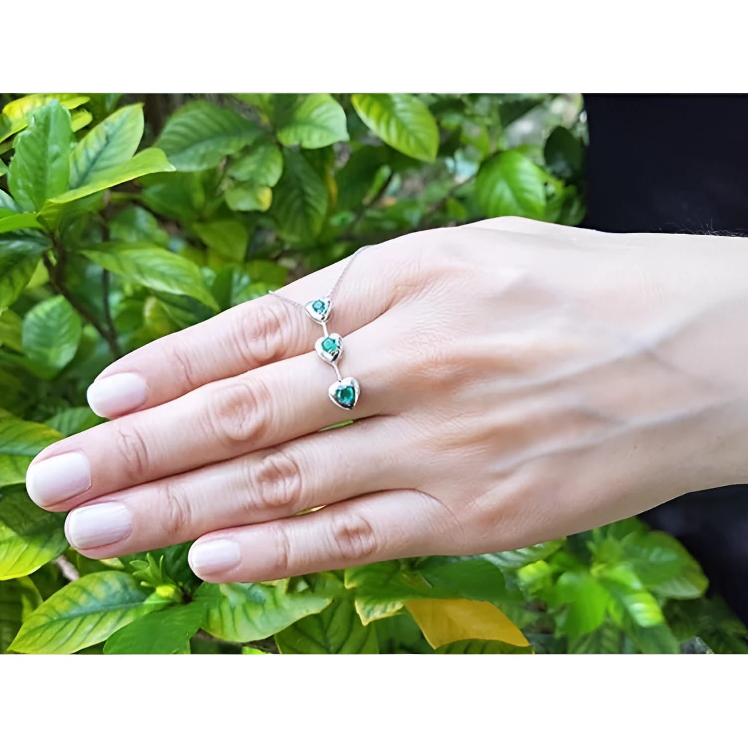 14K white gold journey pendant necklace with three heart-shaped Colombian emeralds on a hand.