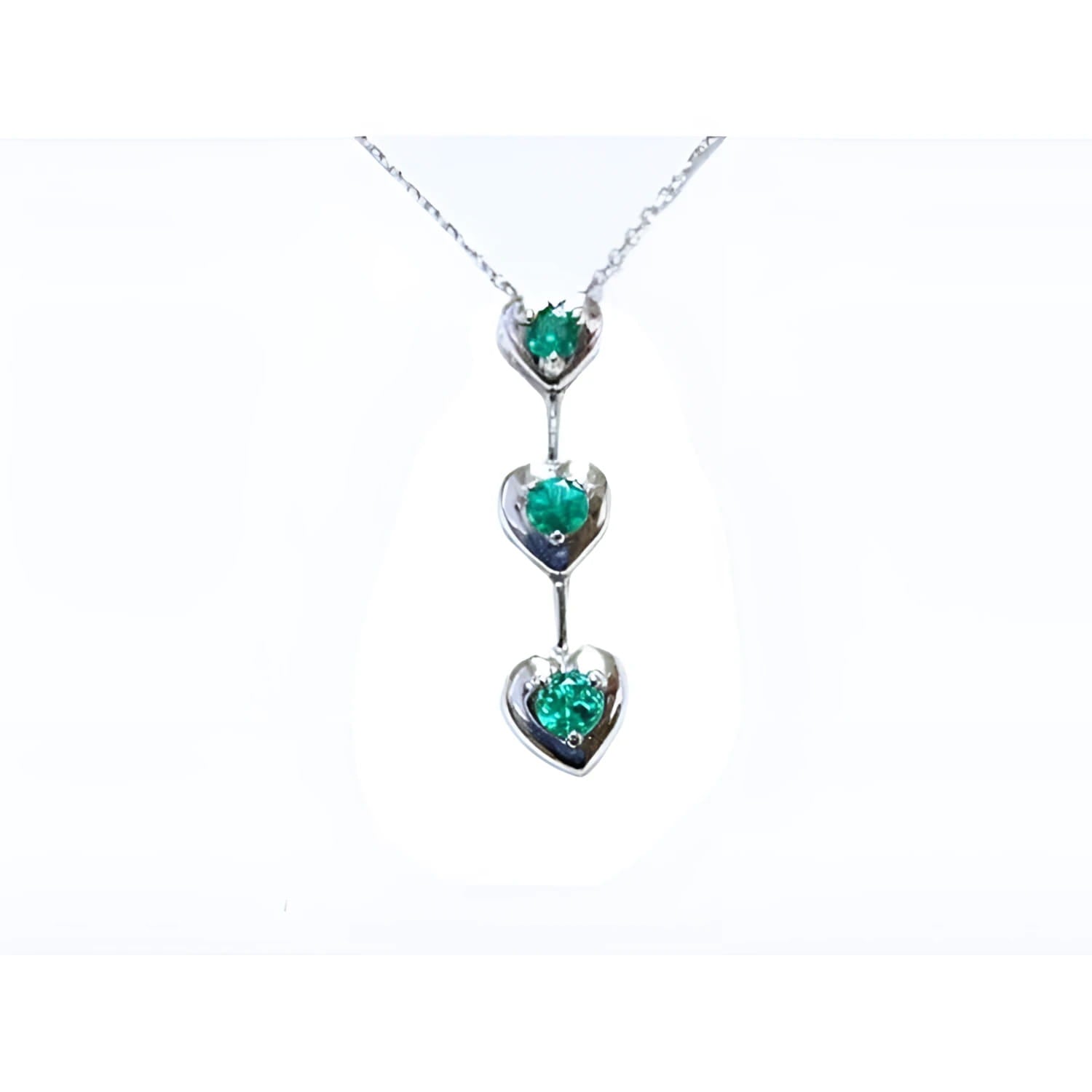 14K white gold journey pendant necklace with three heart-shaped settings, each holding a round green emerald.