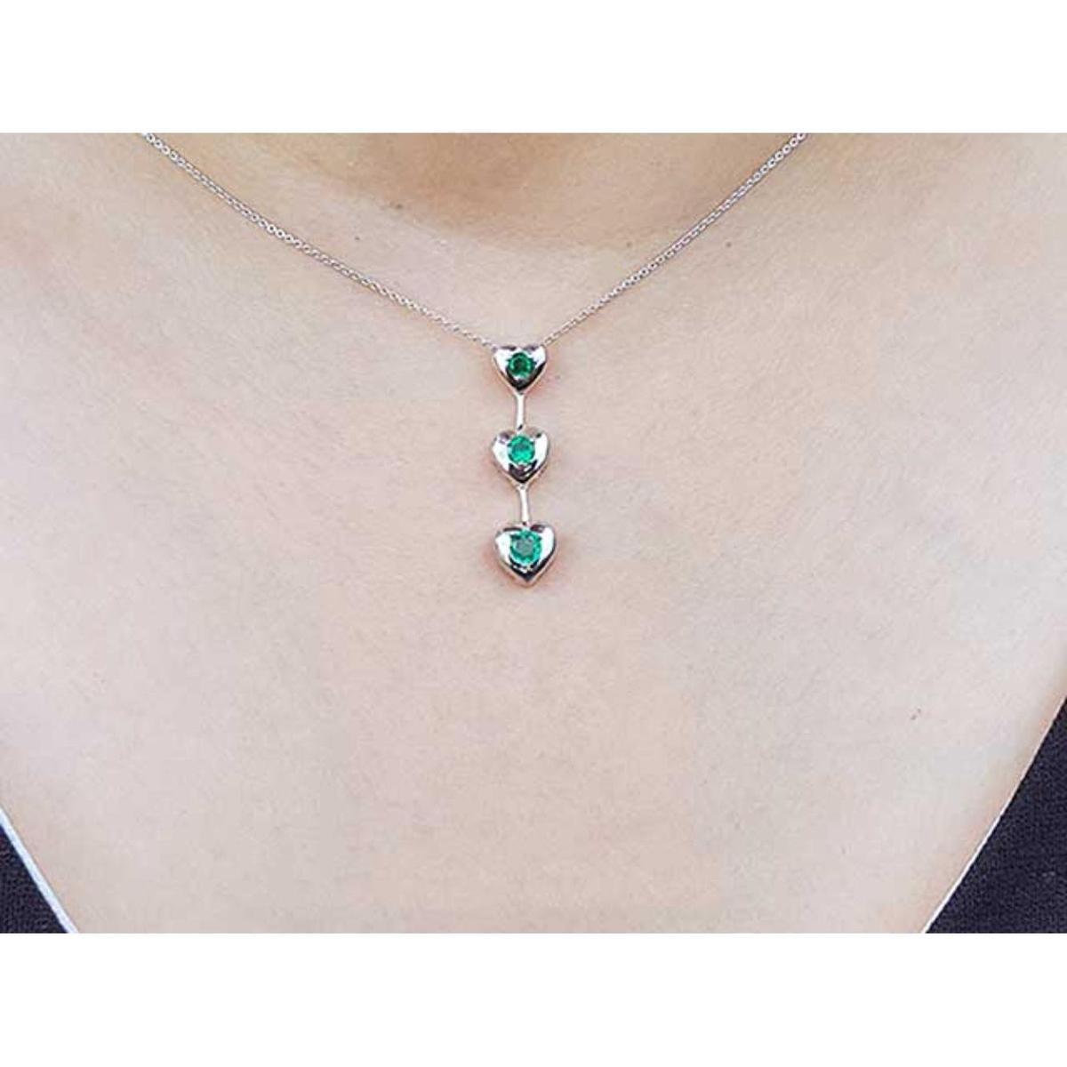 White gold necklace with heart-shaped emerald pendants on a person wearing a light-colored top.