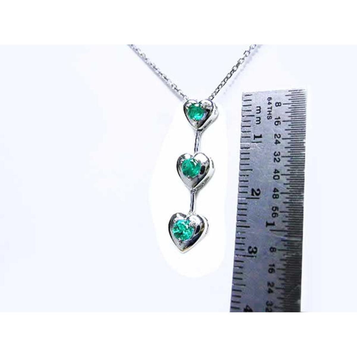 Necklace with heart-shaped pendants featuring natural emeralds, next to a ruler for scale on a white background.
