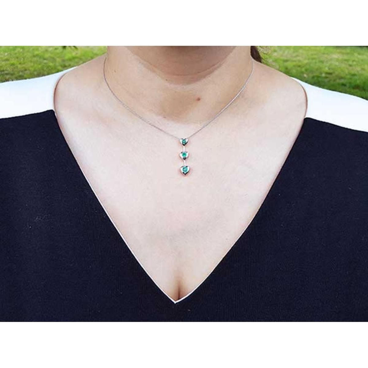 Necklace with three round cut natural emeralds worn by a person in a black top.