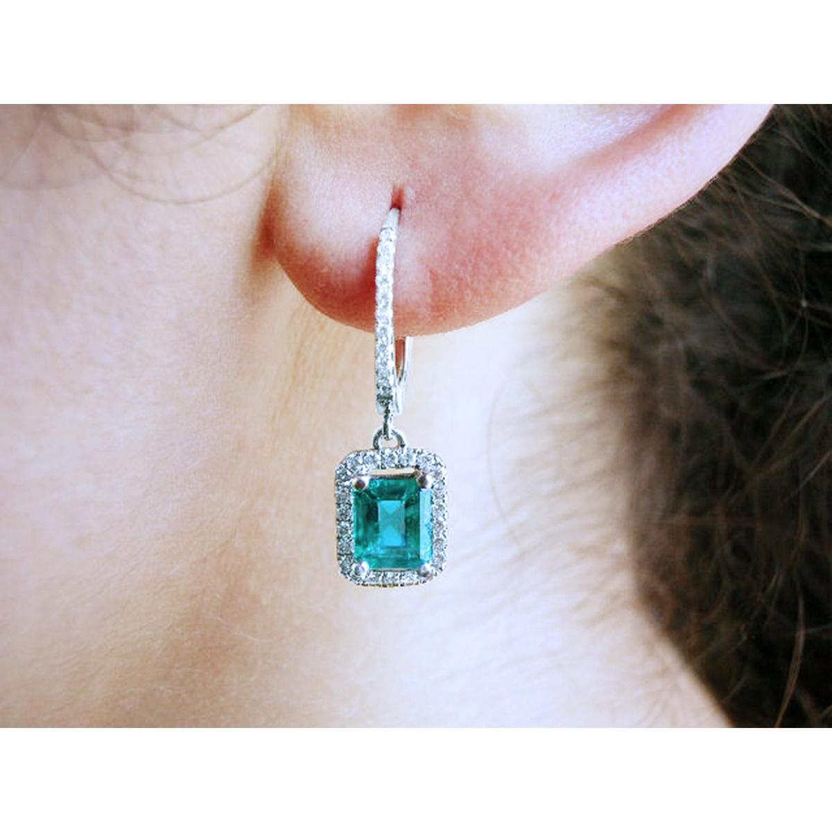 Close-up of a diamond emerald drop earring worn on an ear.
