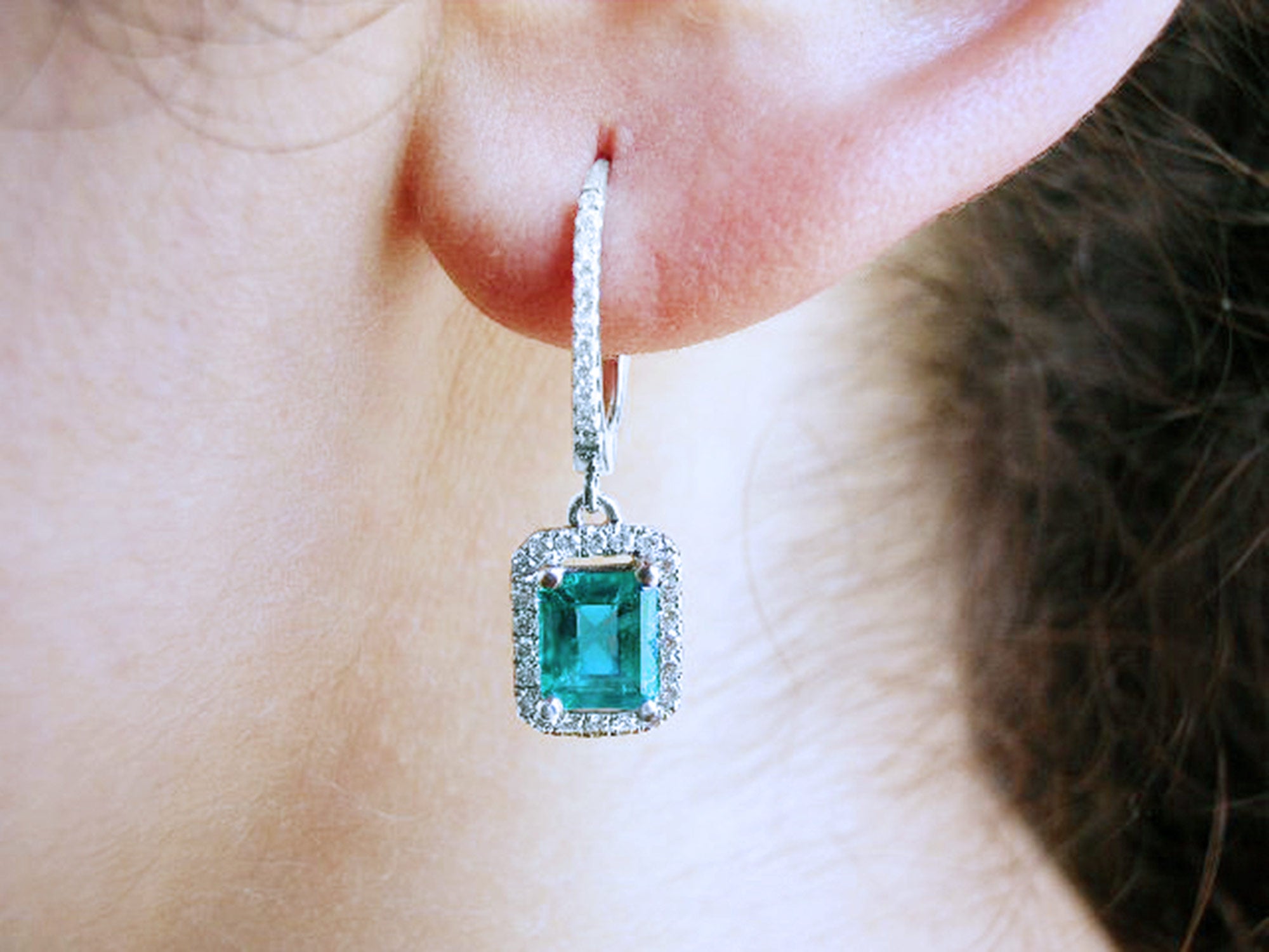 Close-up of a diamond emerald drop earring worn on an ear.