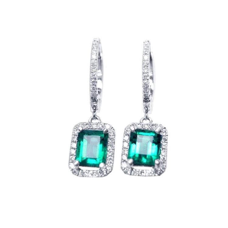 Pair of emerald hoop earrings with diamond accents on a front position, top view.