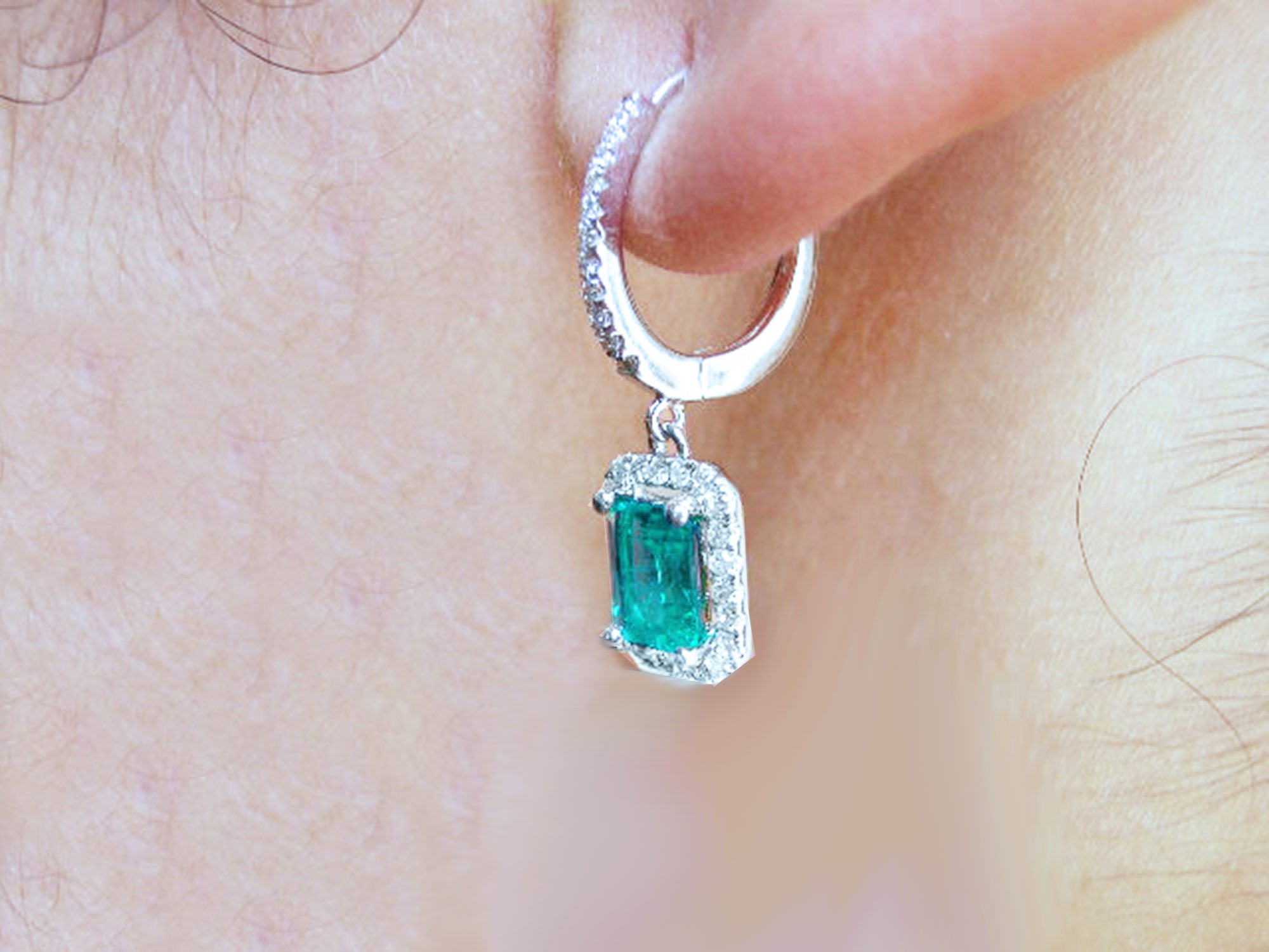 A left side profile of a 14k white gold emerald and diamond hoop earring worn on an ear.