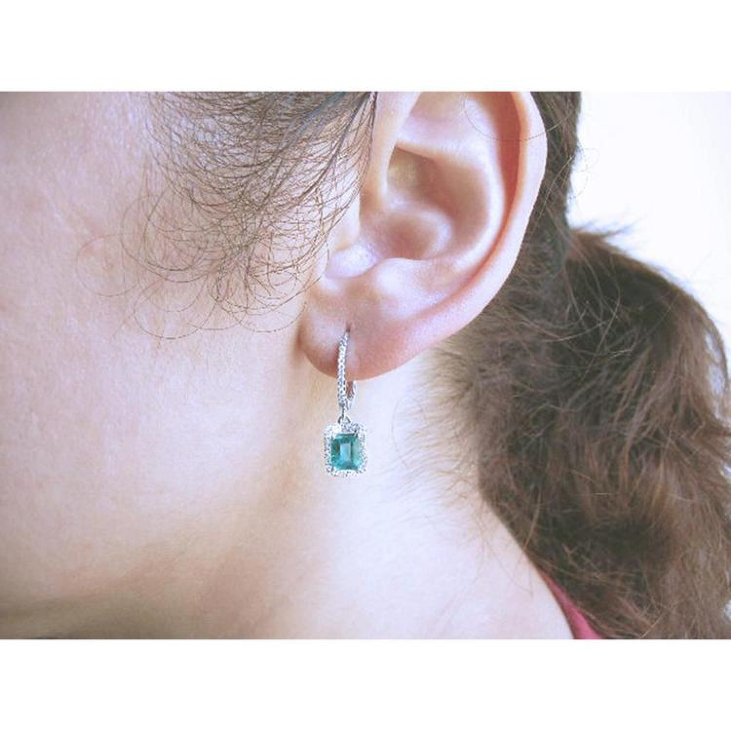 Emerald dangle hoop earrings with diamonds in 14k white gold on an ear.