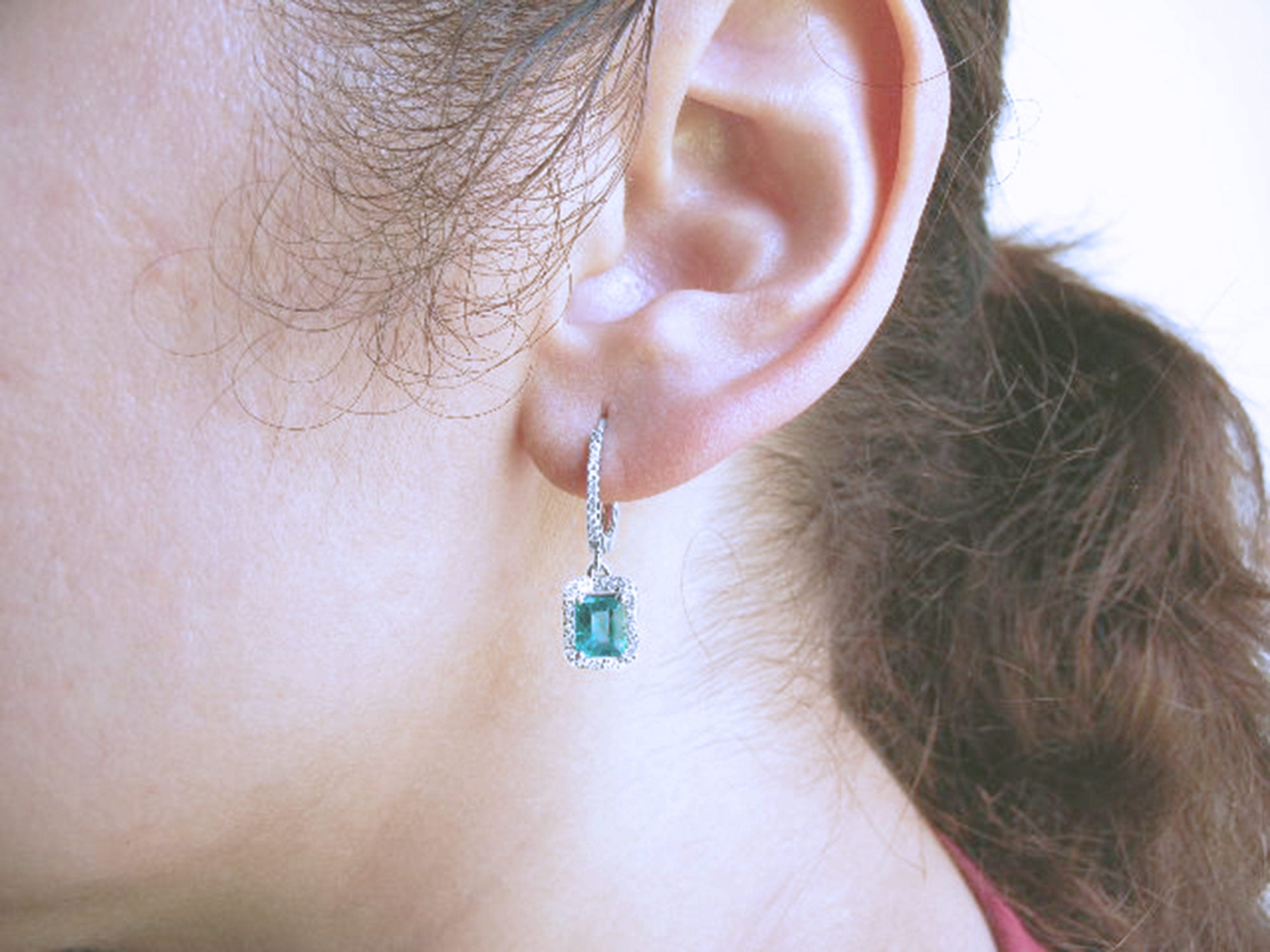 Close-up of an ear wearing a natural emerald hoop earring with a blurred background.