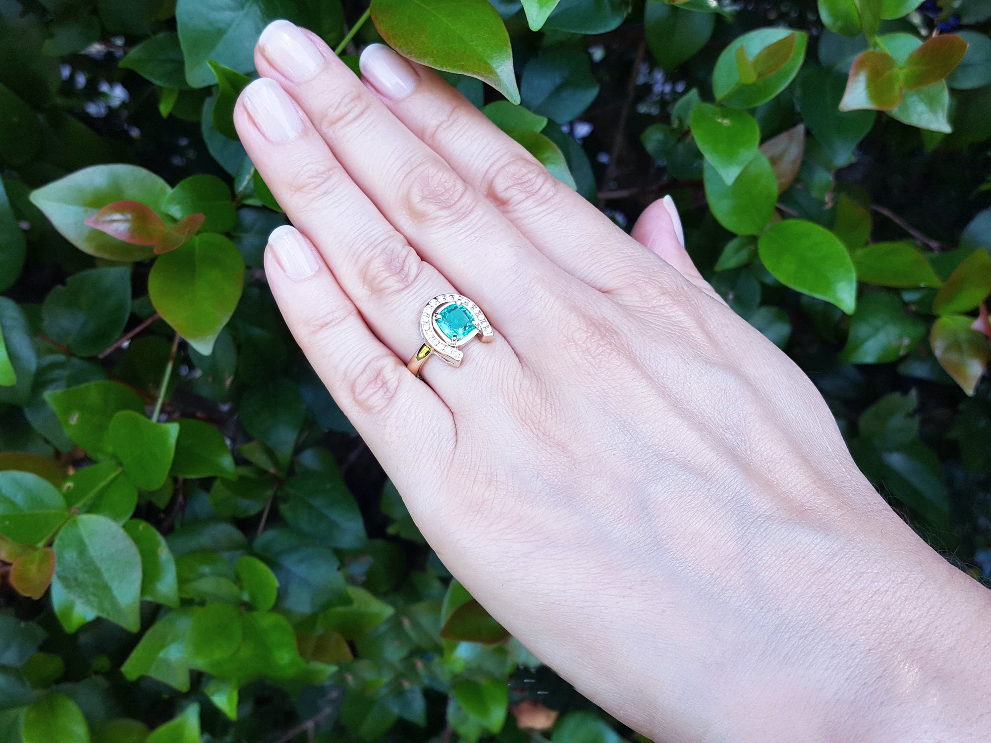 A hand wearing a horseshoe emerald ring for women crafted in 14k yellow gold