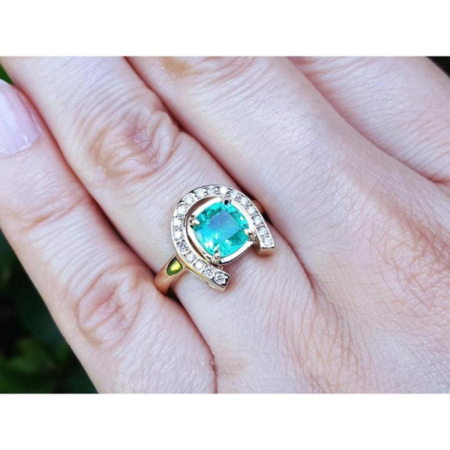 14K yellow gold horseshoe ring with a cushion-cut emerald and diamond halo, worn on a hand.