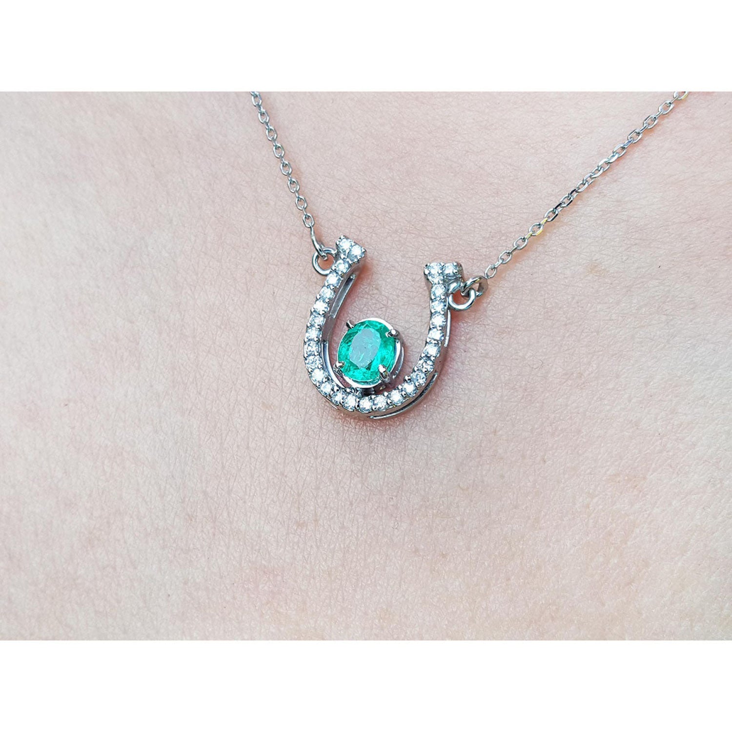 14K white gold horseshoe necklace with a prong-set oval emerald and natural diamonds.