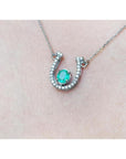 14K white gold horseshoe necklace with a prong-set oval emerald and natural diamonds.