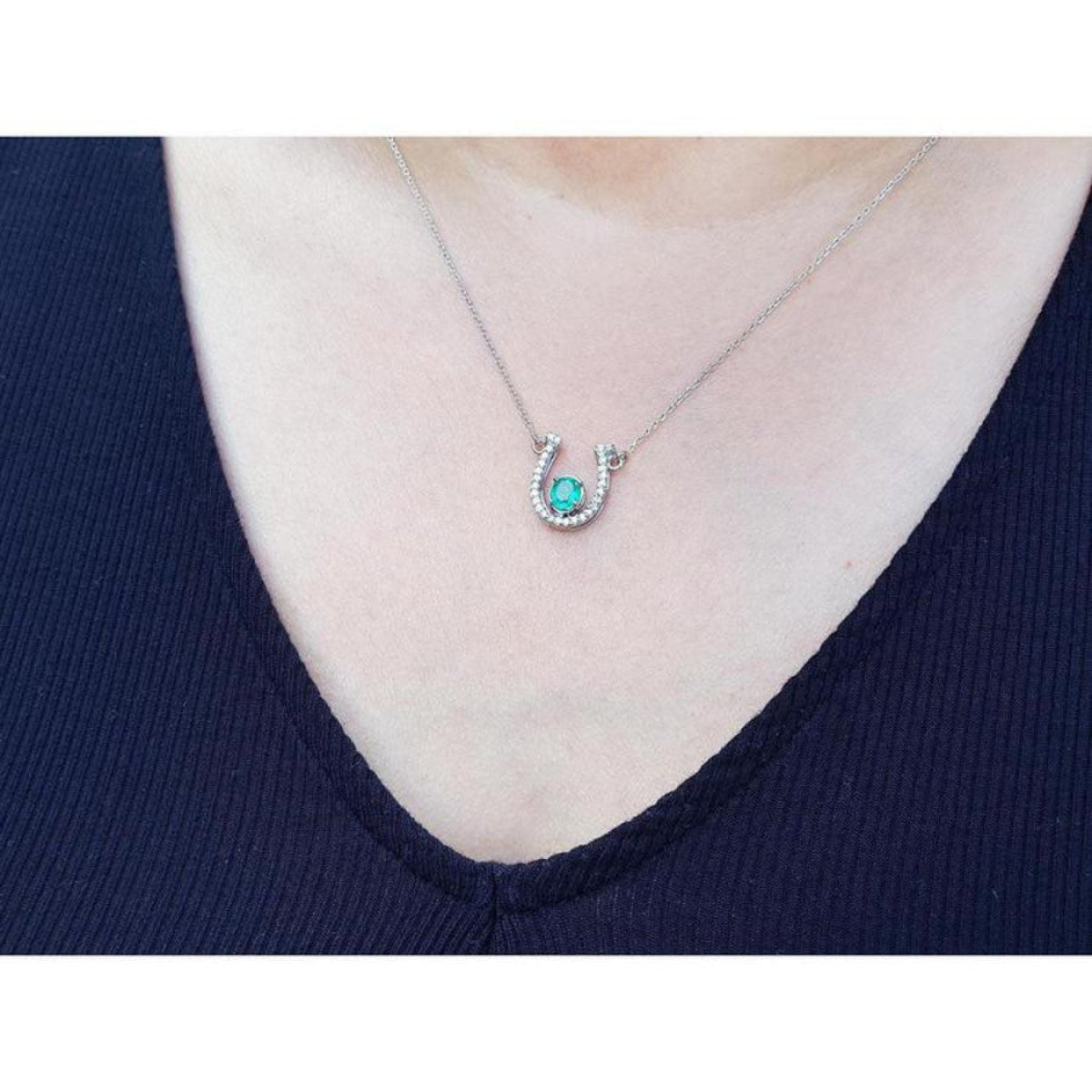 White gold oval emerald horseshoe necklace with diamonds, worn on a person.
