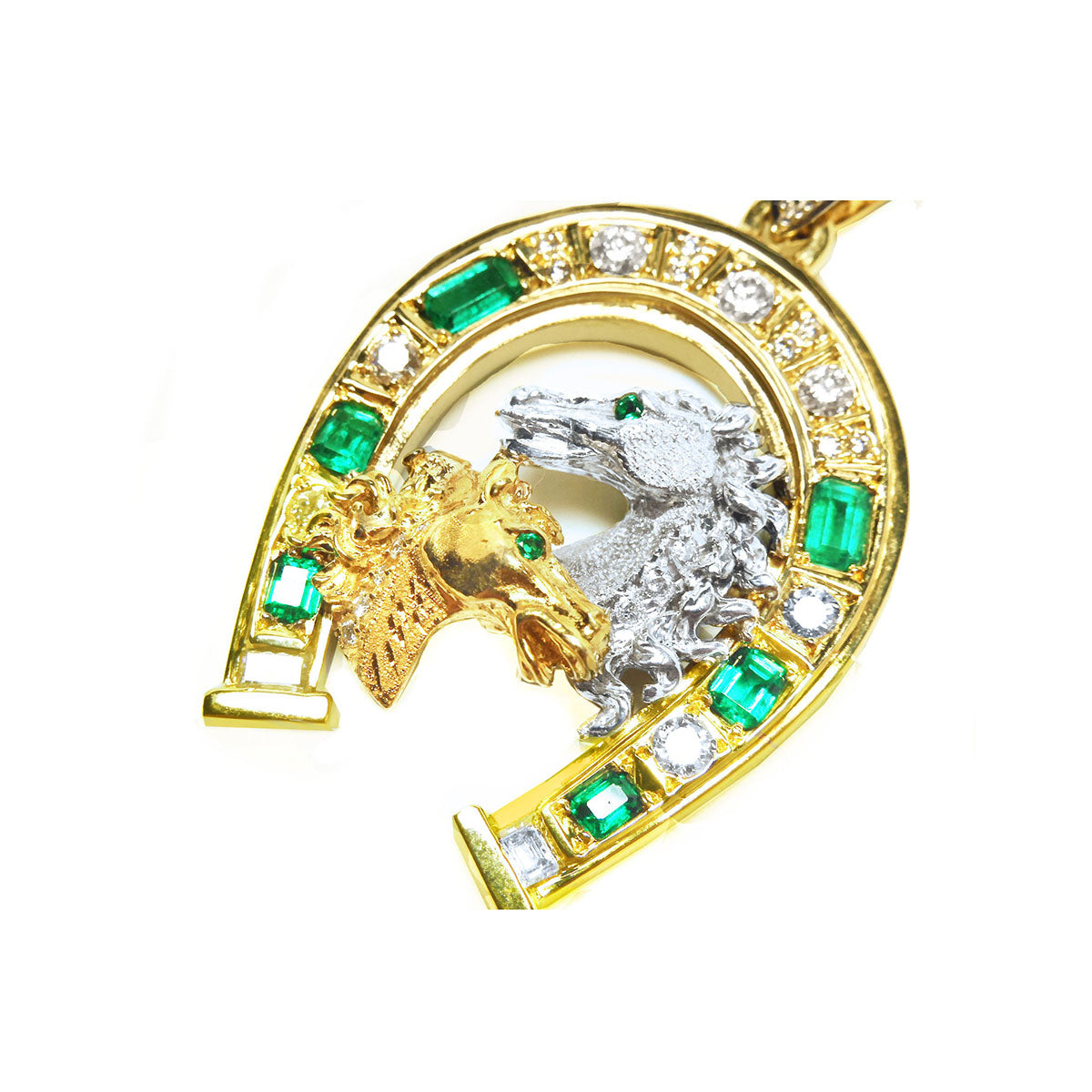 A yellow and white gold horse heads pendant with natural emeralds and diamonds on a white background