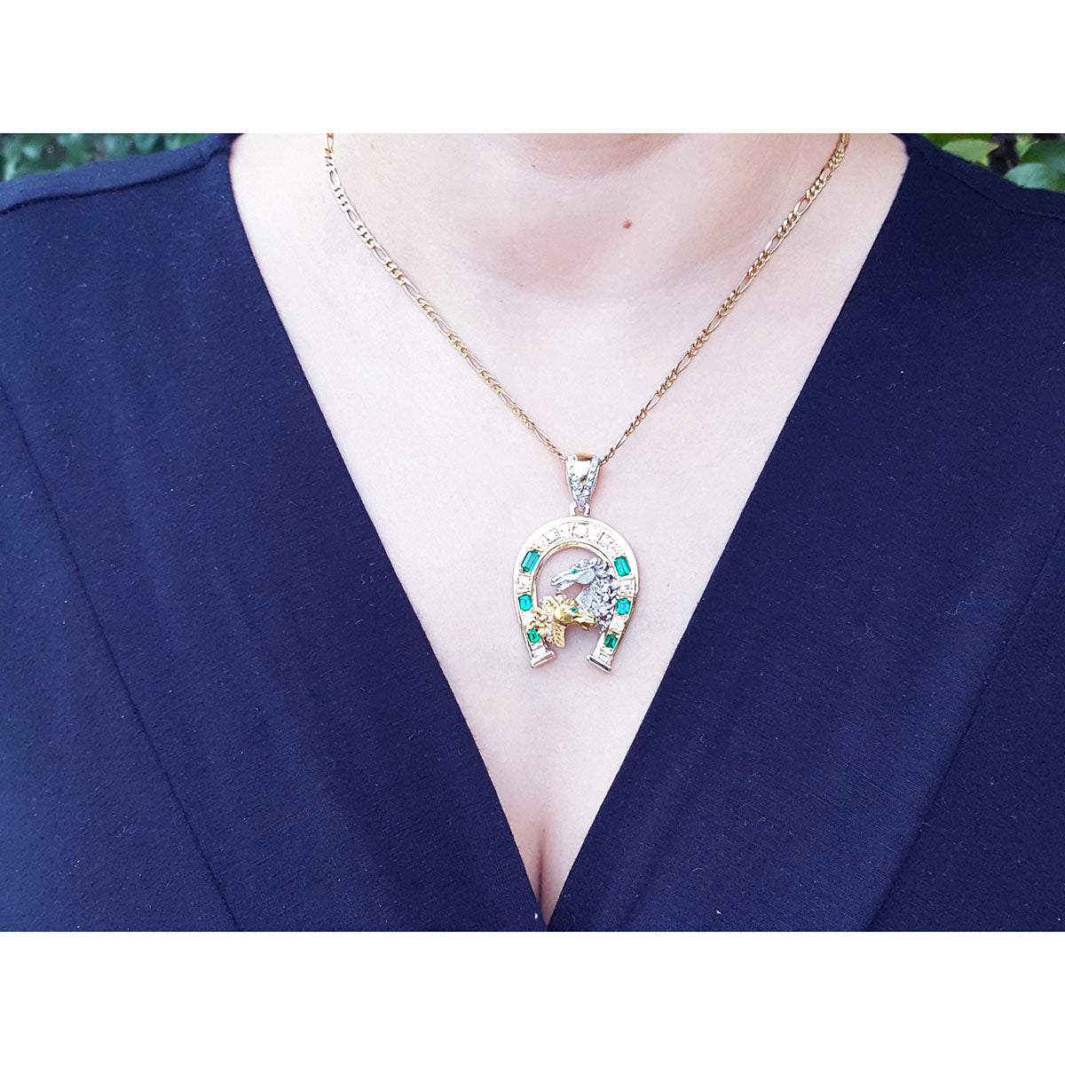 Necklace with a horseshoe emerald and diamond pendant on a person wearing a blue top.