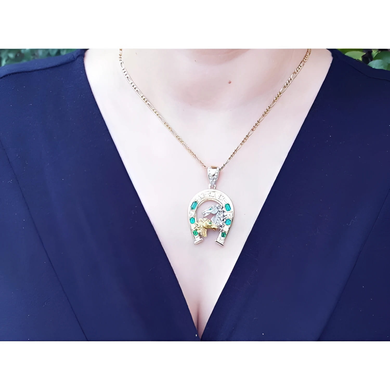 18K yellow gold horseshoe pendant with Colombian emeralds on a chain, worn on a dark shirt.