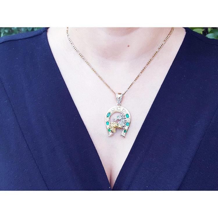 Necklace with a horseshoe emerald and diamond pendant on a person wearing a blue top.