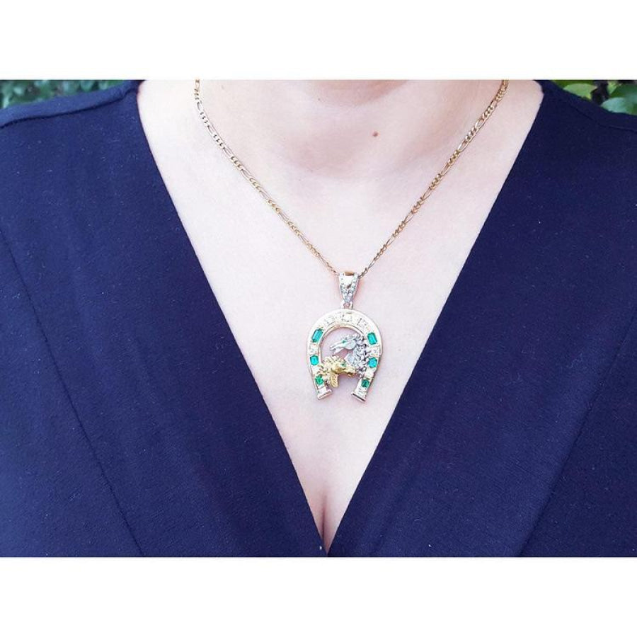 18K yellow gold horseshoe pendant with Colombian emeralds on a chain, worn on a dark shirt.