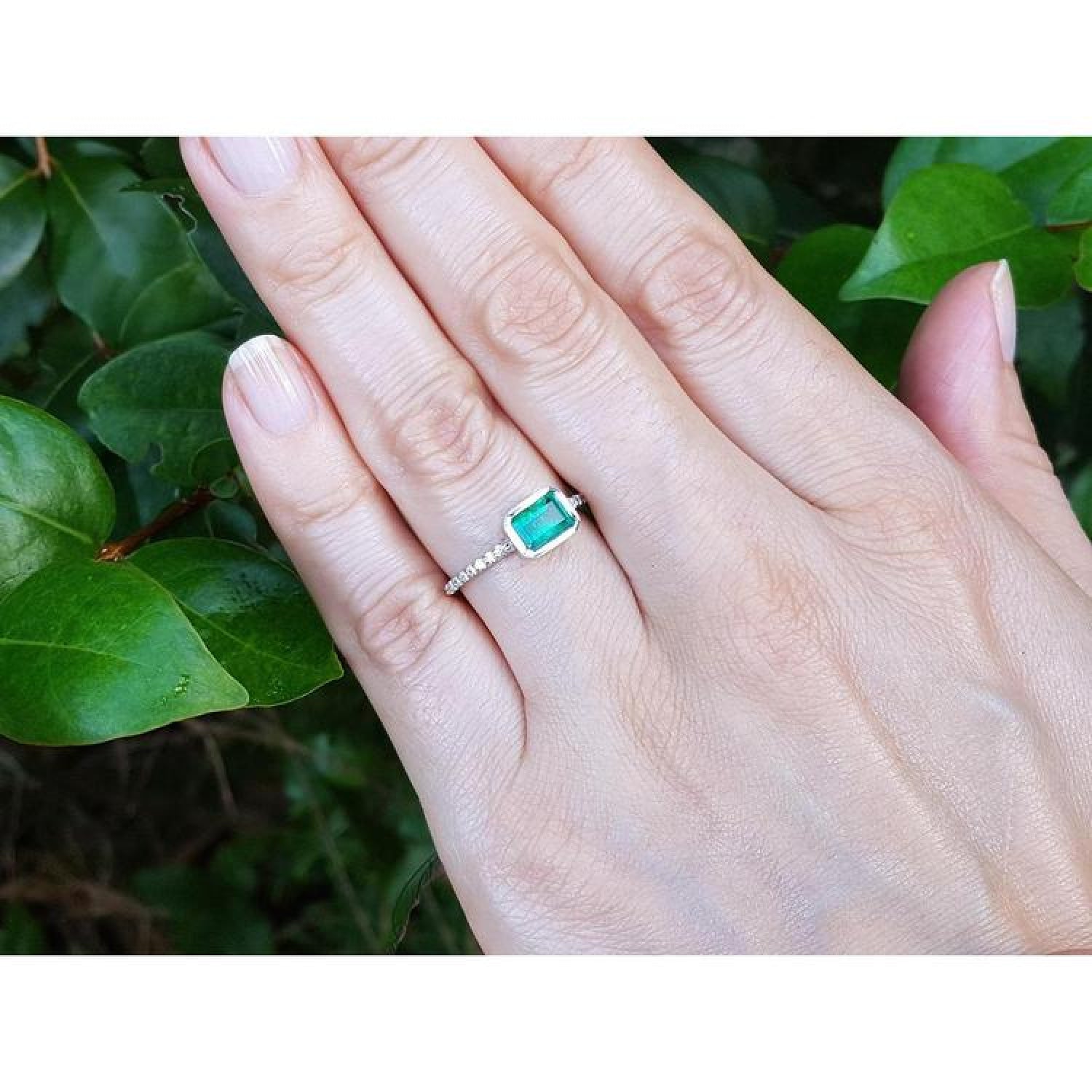 Hand wearing a 14K white gold ring with a bezel-set emerald and prong-set accent diamonds.