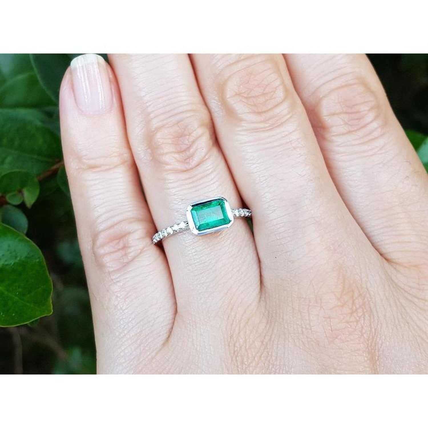0.73 ct bezel-set emerald ring with accent diamonds on a 14K white gold band worn on a hand.