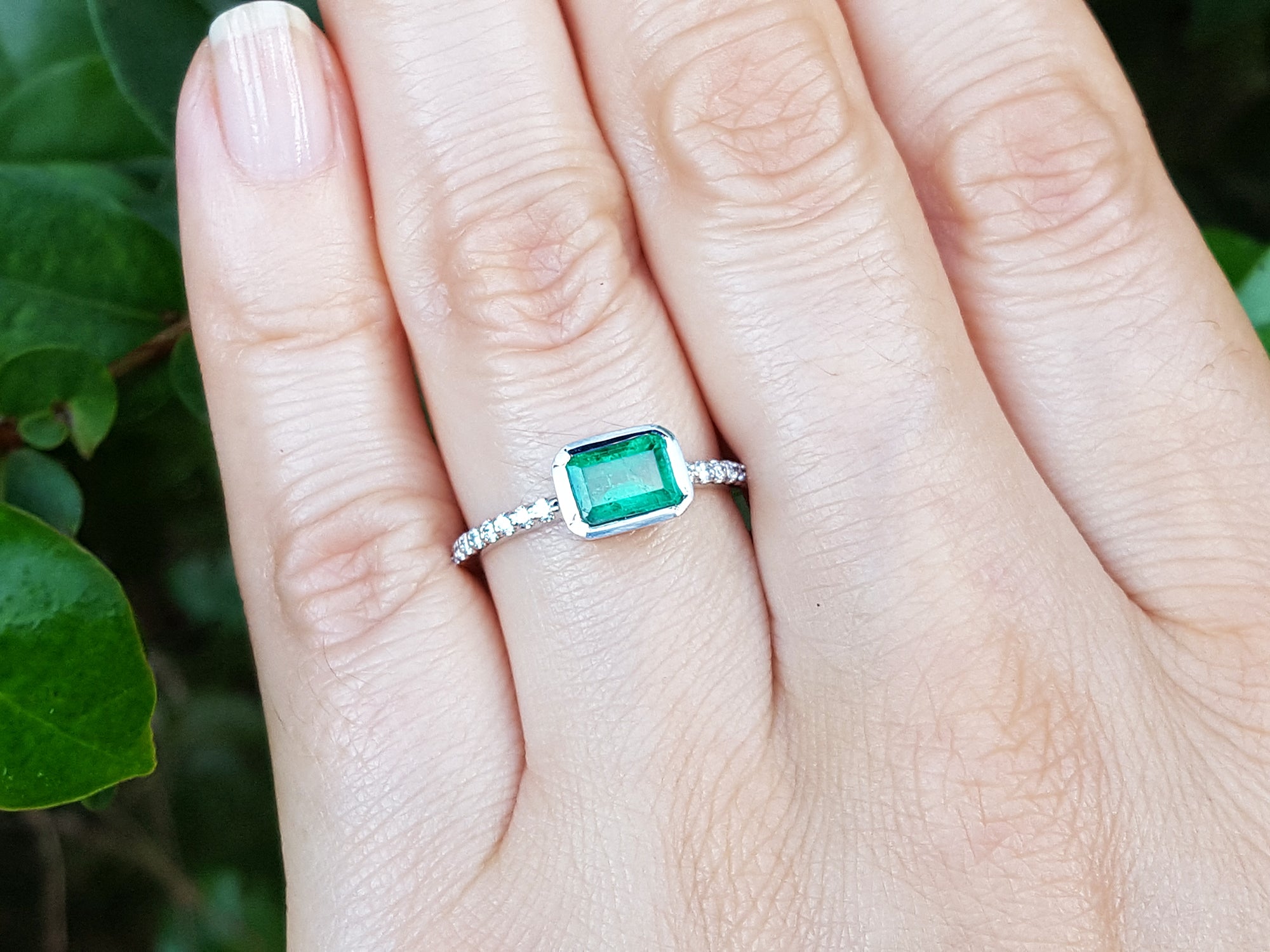 Hand wearing a genuine emerald ring white gold against a natural background.