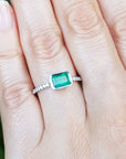 Hand wearing a genuine emerald ring white gold against a natural background.