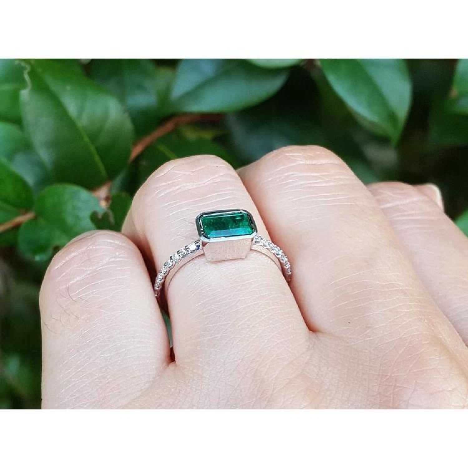 0.73 ct bezel set emerald ring with accent diamonds on a 14K white gold band, worn on a finger.