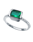 The tilted position of this bezel set emerald ring reveals the top setting, a portion of the gallery, and the band design.