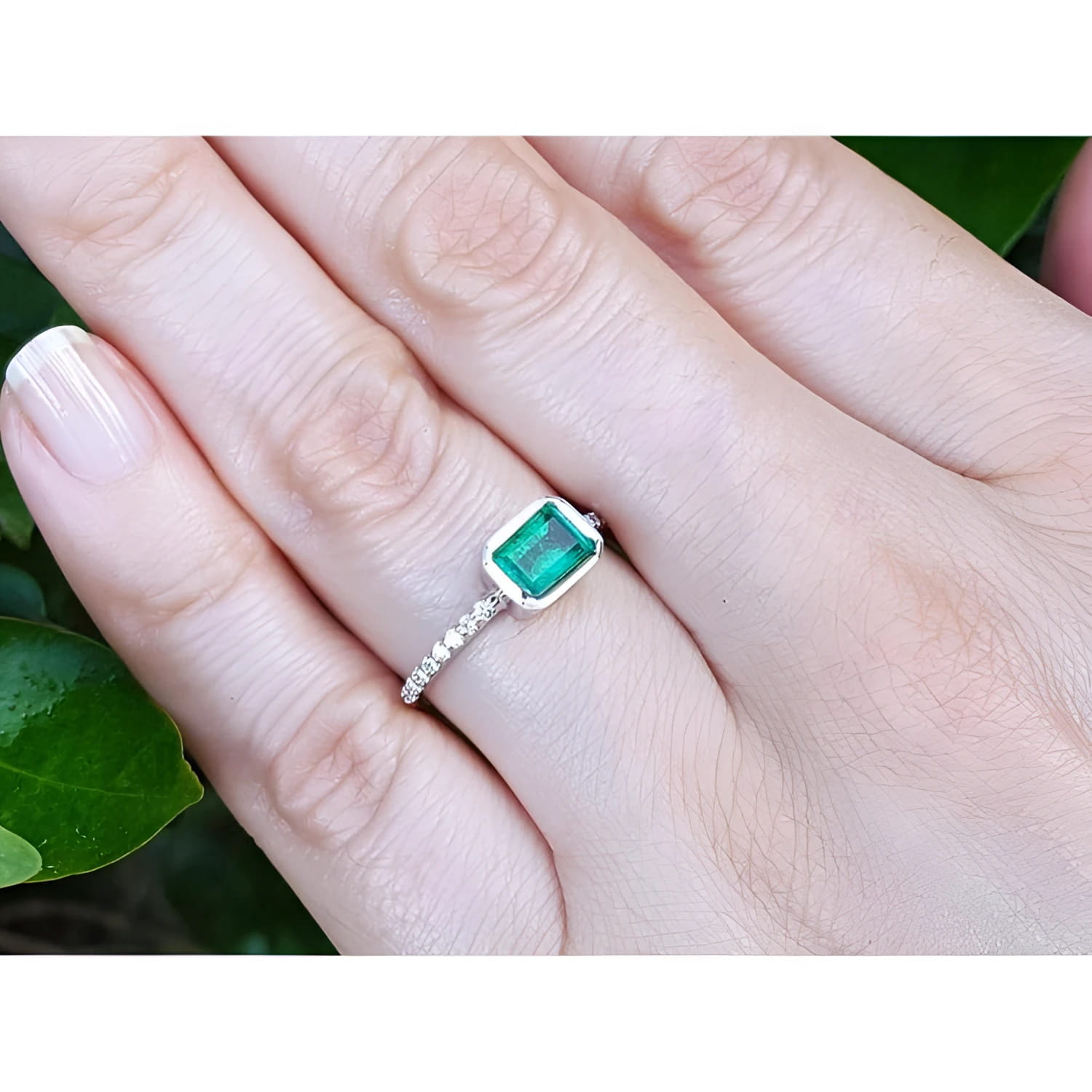Hand wearing a bezel set emerald ring for women in 14k white gold