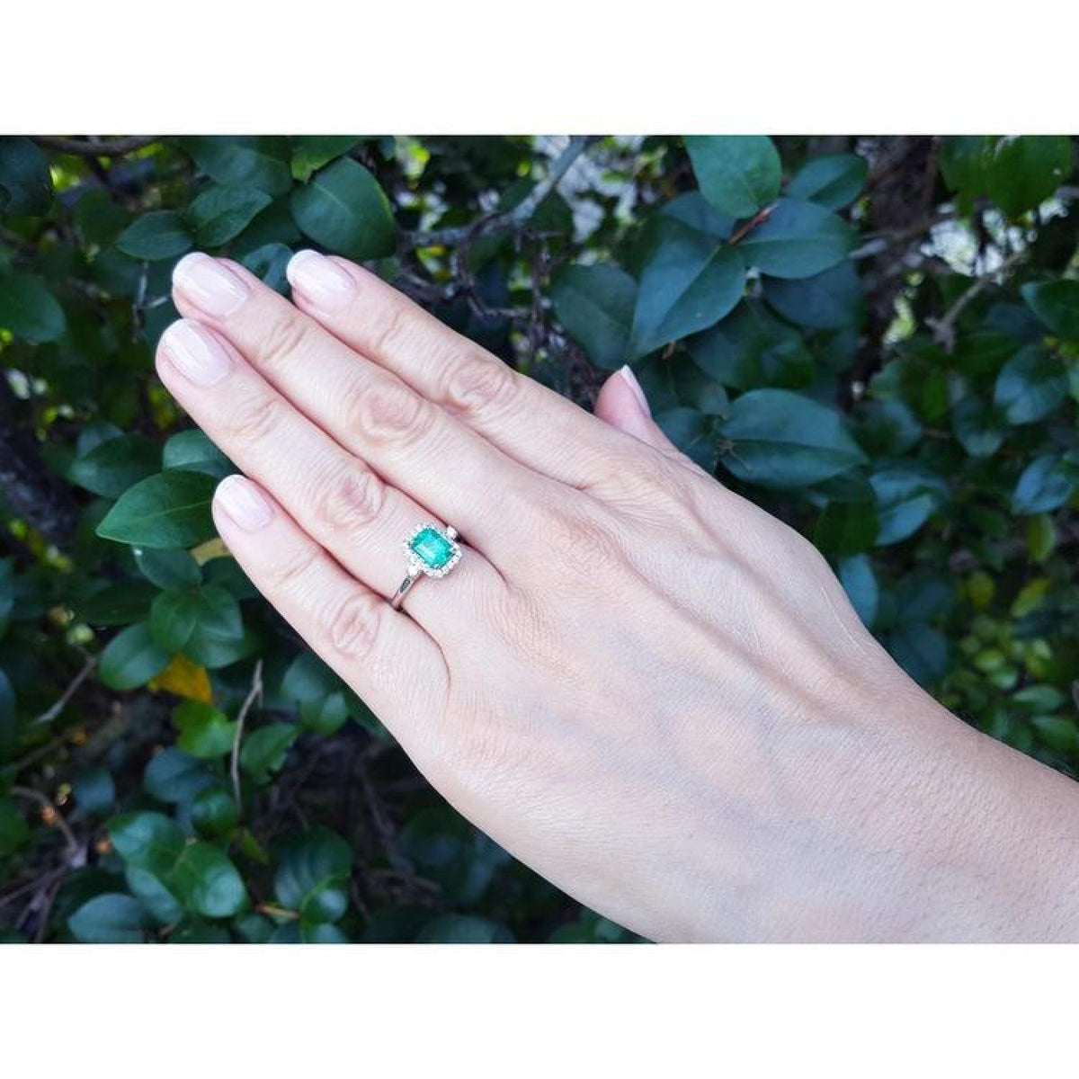 Emerald cut emerald engagement ring with diamond halo in 14K white gold on a hand.