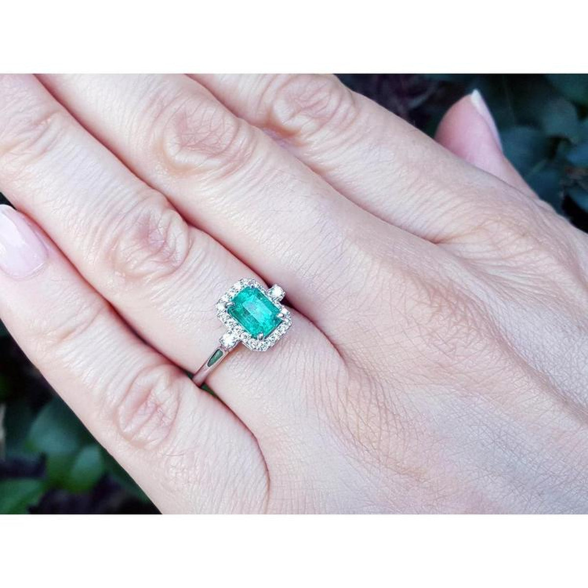 1.47 ct emerald cut emerald engagement ring with diamond halo in 14K white gold on a hand.