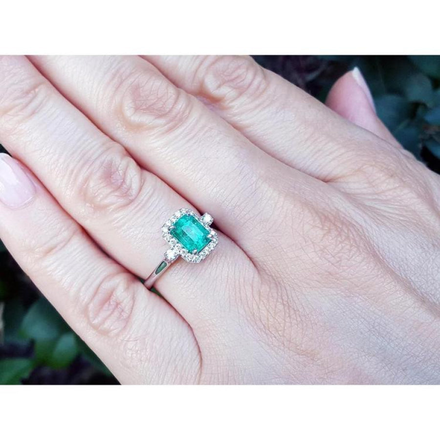 1.47 ct emerald cut emerald engagement ring with diamond halo in 14K white gold on a hand.