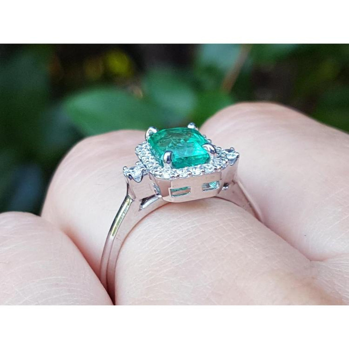 14K white gold emerald cut emerald ring with diamond halo on a finger.