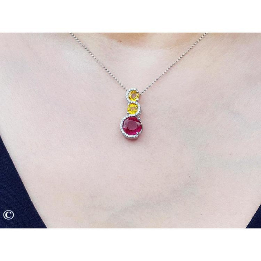 14K white gold ruby journey pendant with round ruby, two yellow sapphires, and diamond accents.