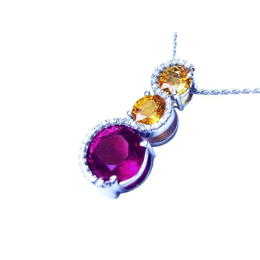 14K white gold journey pendant with a round ruby, two yellow sapphires, and diamond accents.