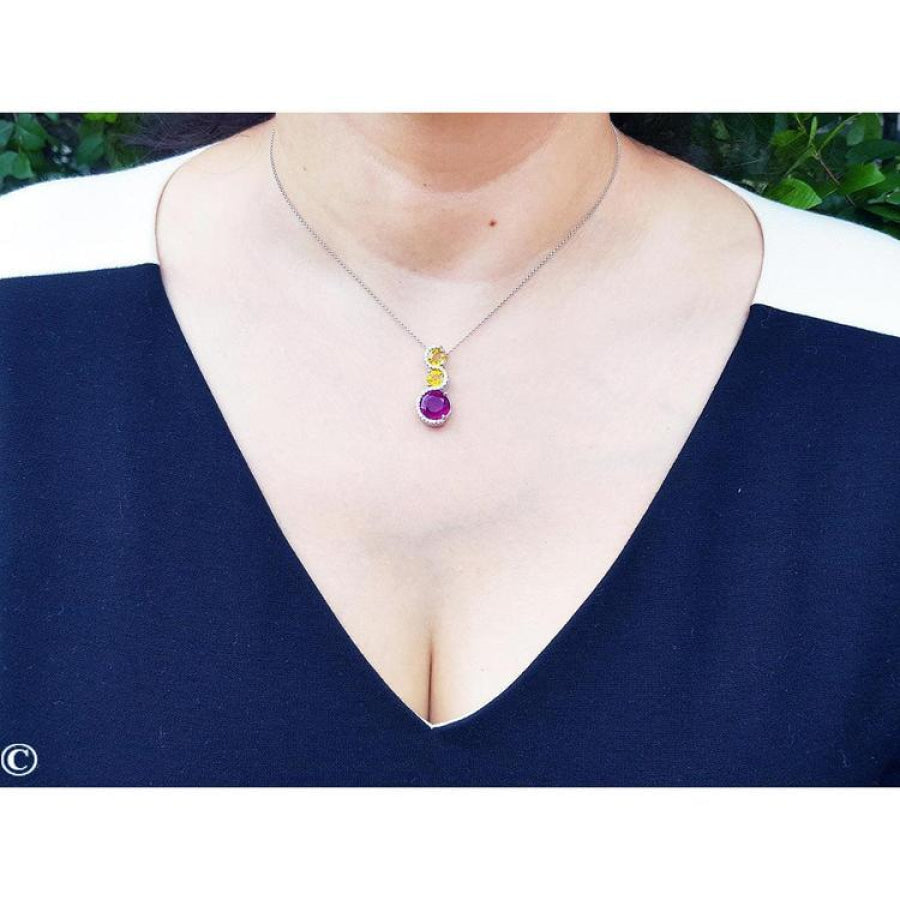 14K white gold journey pendant with a round ruby, two yellow sapphires, and diamonds on a woman's neck.
