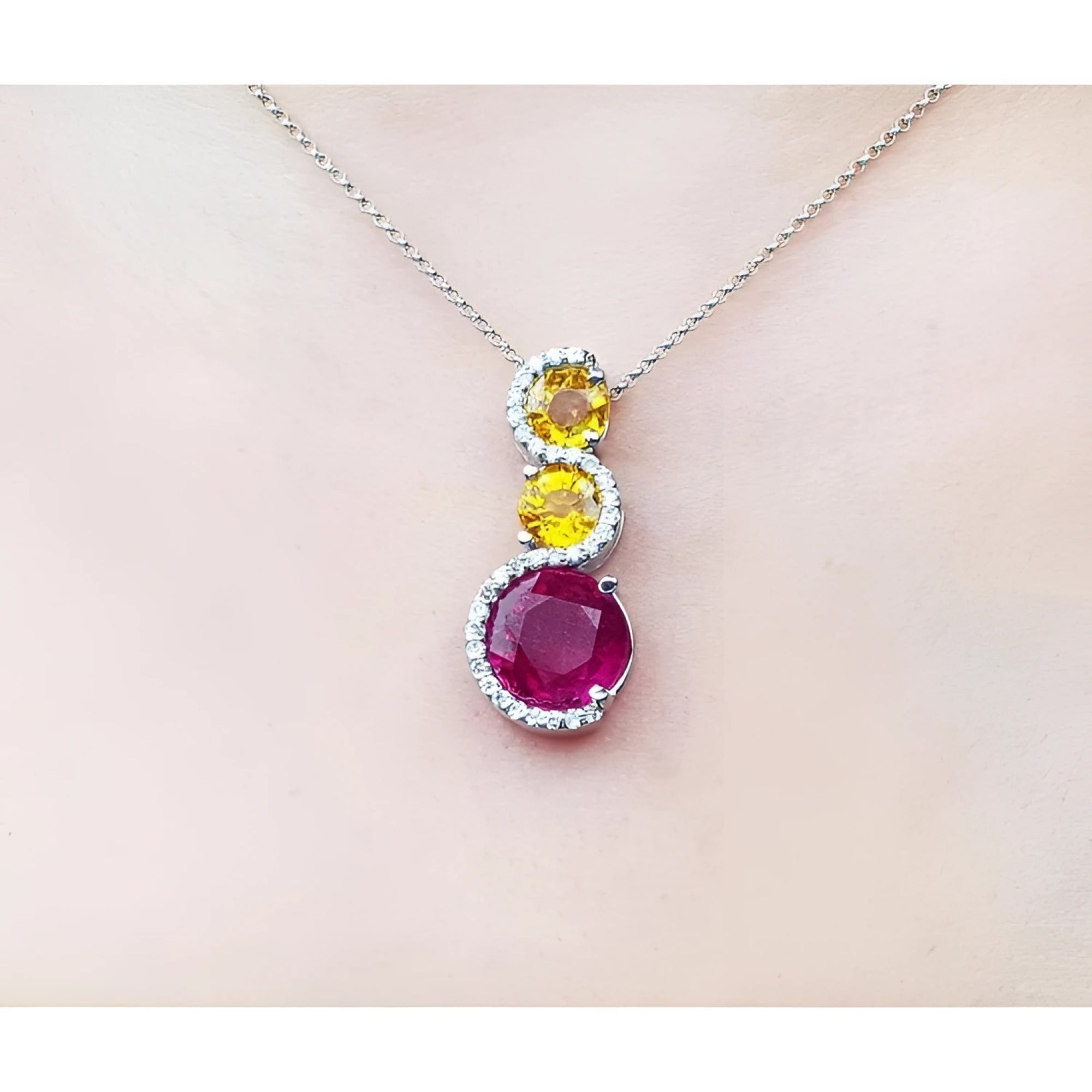 14K white gold journey pendant with a round ruby, two yellow sapphires, and diamond accents on a chain.
