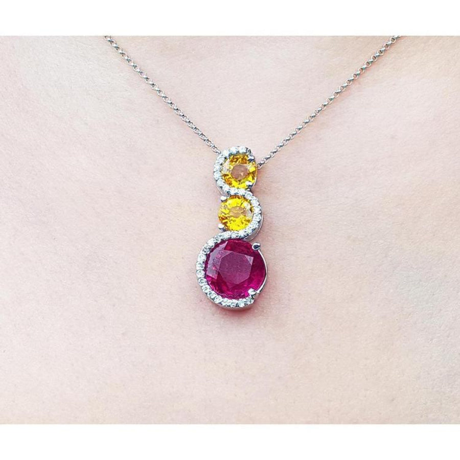14K white gold journey pendant with a round ruby, two yellow sapphires, and diamond accents on a chain.