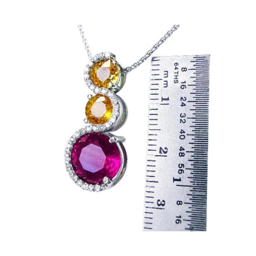 14K white gold journey pendant with a round ruby, two yellow sapphires, and diamond accents.