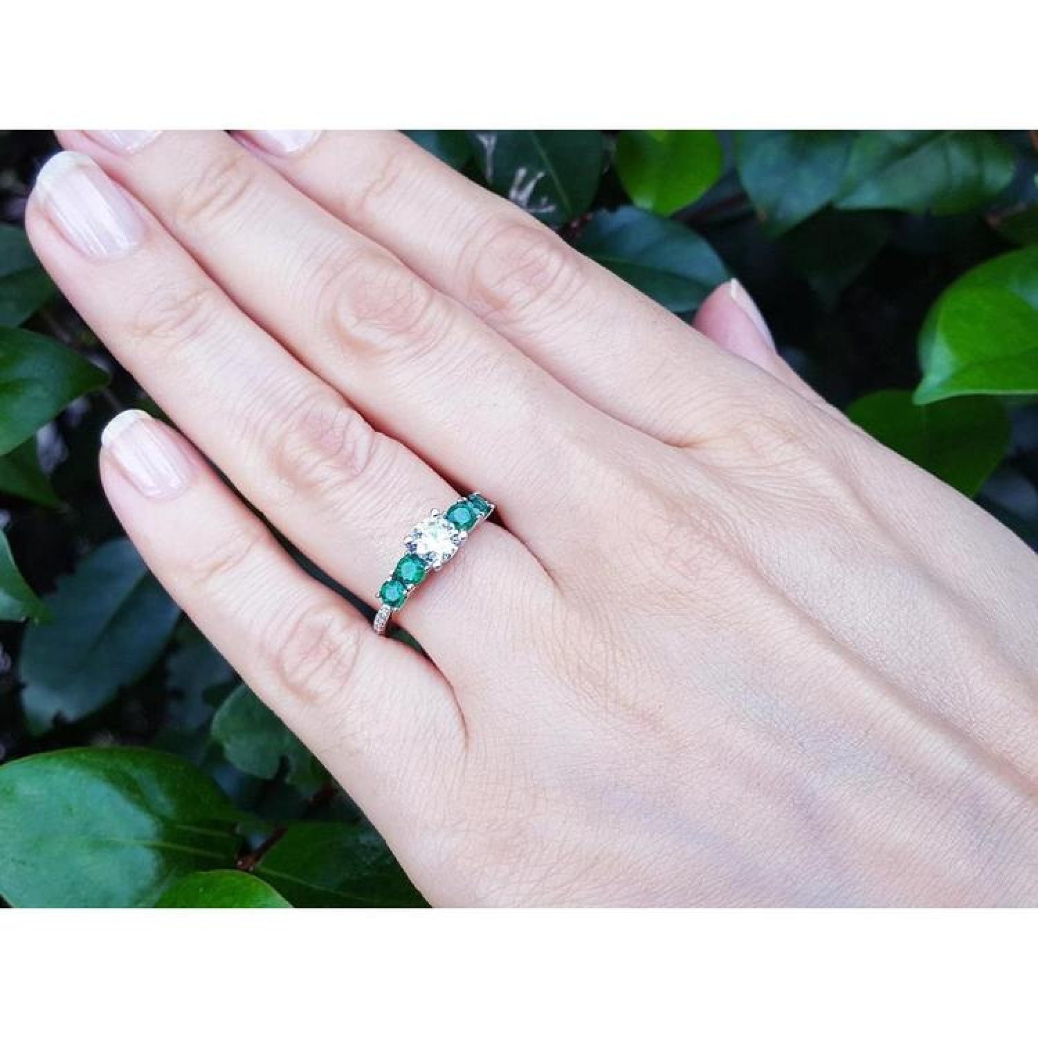 14K white gold ring with a round natural diamond center and four side emeralds on a hand.