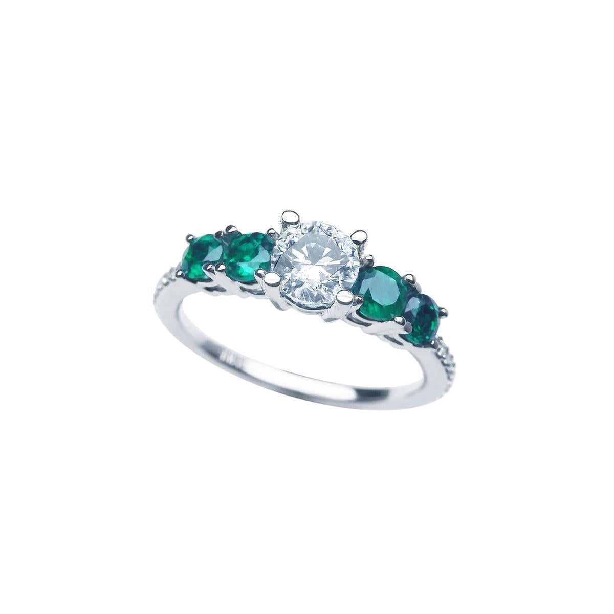 A tilted position of this ring with a round cut diamond and side emeralds displays its topside. 