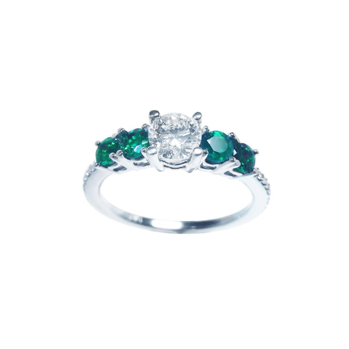 This ladies' ring with a center diamond round cut and side emeralds displays top and sides profile.