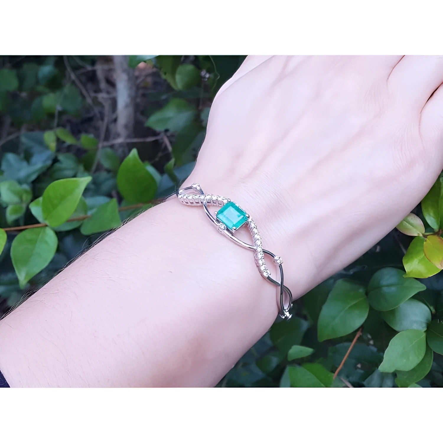 Emerald bangle bracelet with natural diamonds in 14K white gold, worn on a wrist.