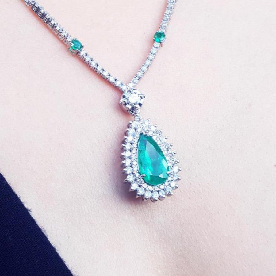 Pear cut emerald necklace with double diamond halo, 18K white gold chain with emerald accents.