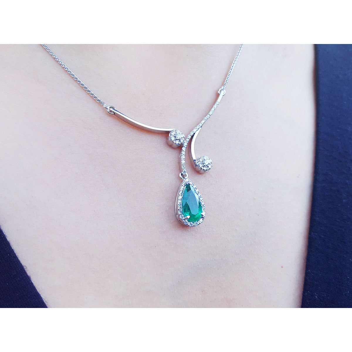18k white gold necklace with a teardrop natural emerald pendant halo diamond on a person&#39;s neck 