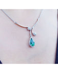 18k white gold necklace with a teardrop natural emerald pendant halo diamond on a person's neck 