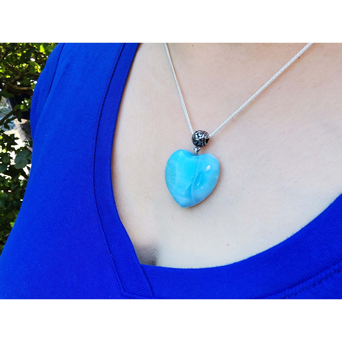 Person wearing a blue heart-shaped larimar pendant necklace with a blue top.