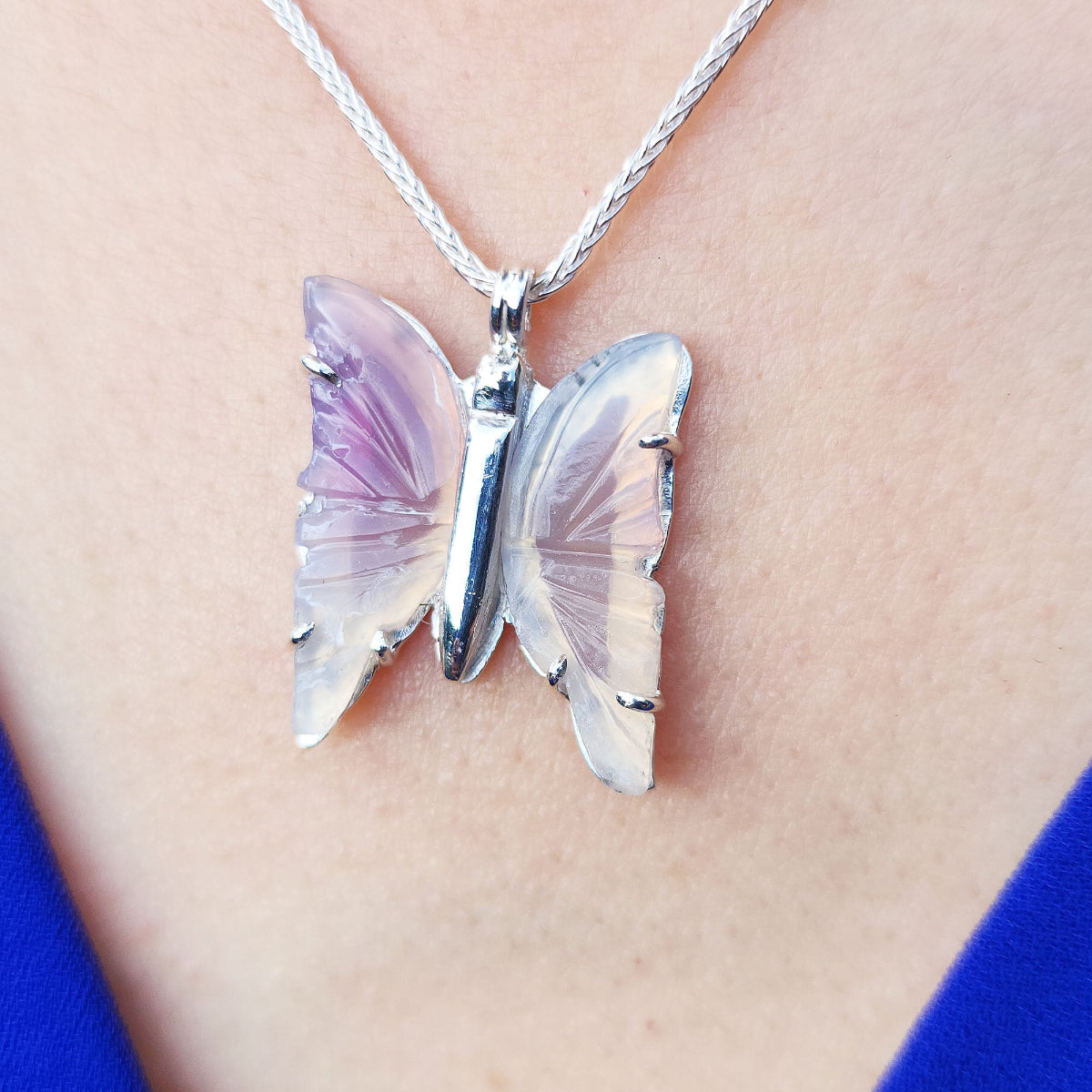 An agate butterfly-shaped pendant on a necklace worn by a person with a blue garment visible.