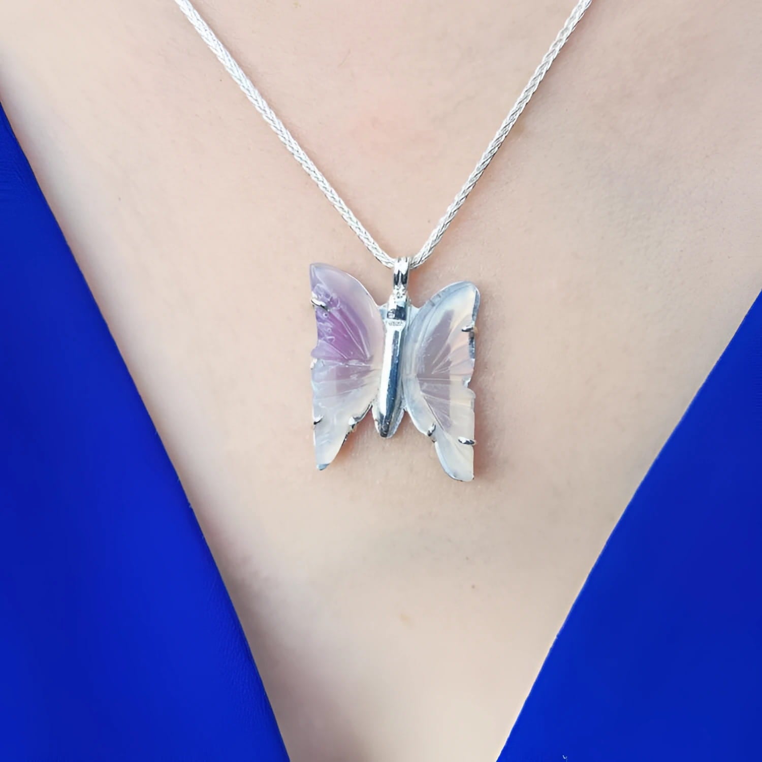 Lavender agate butterfly pendant necklace with sterling silver chain on a blue top.