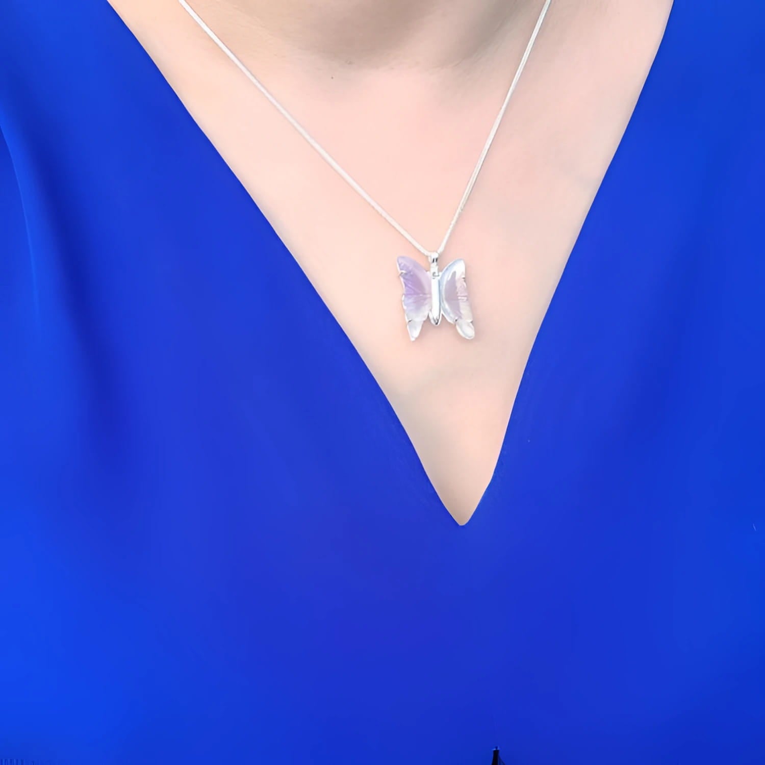 Lavender agate butterfly pendant necklace with sterling silver chain on a blue top.
